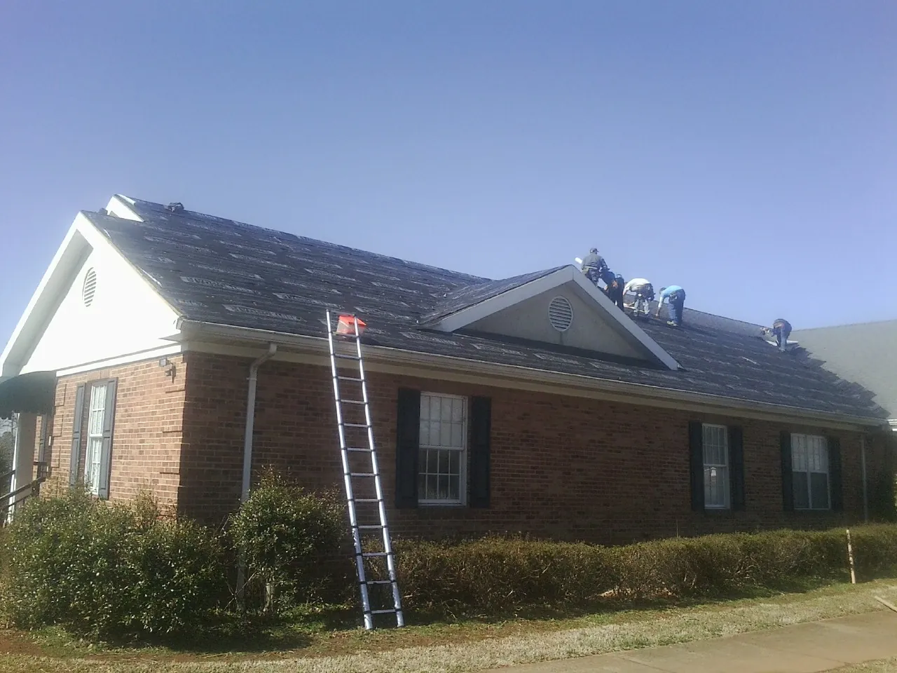 Crew tearing shingles off a brick ranch roof with a ladder set — Metal Roof Repair work by our crew in Georgetown